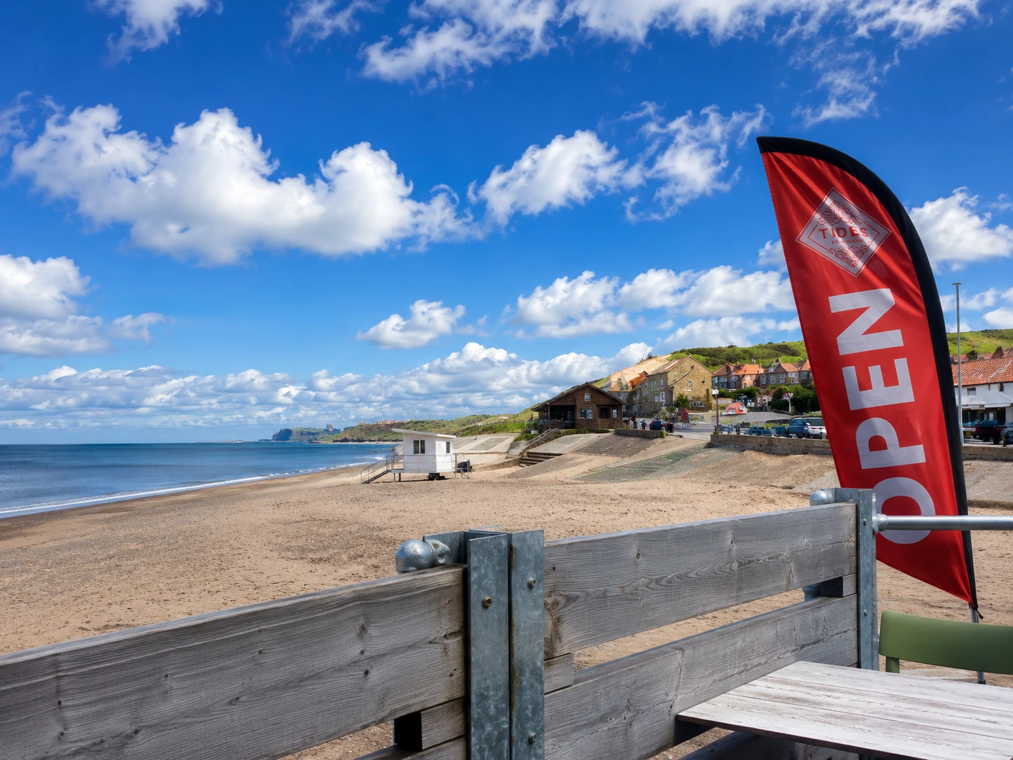 The red Tides flag beside outdoor seating with Sandsend beach beyond